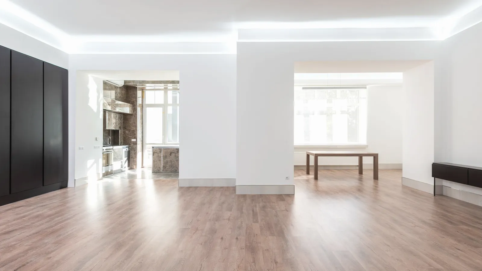 A bright empty room with a wooden floor and a tall window.