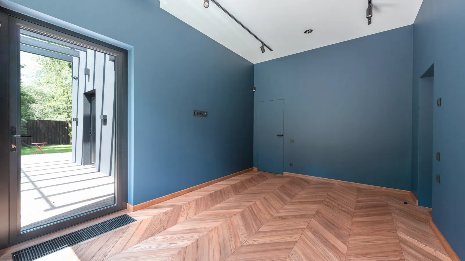 A room with deep blue walls, a wooden floor and a large window.
