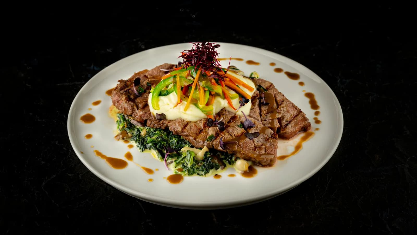 A steak course with herbs and jus on dark stone.