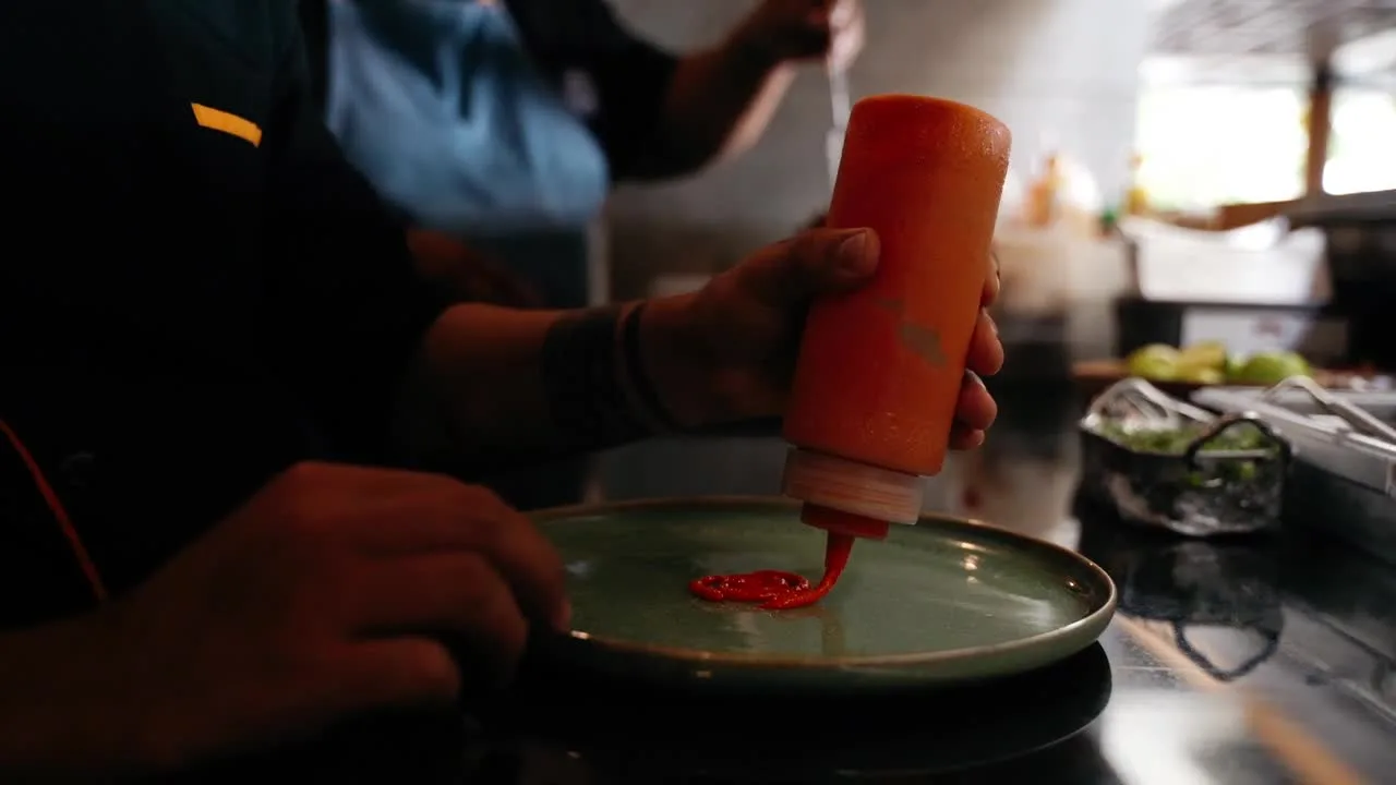 A cook drawing a line of sauce across a plate with a squeeze bottle.
